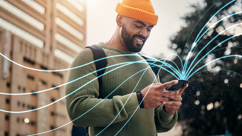 A man in a green sweater and orange knit cap is enjoying several Usenet connections that are coming out of his phone as blue ribbons.