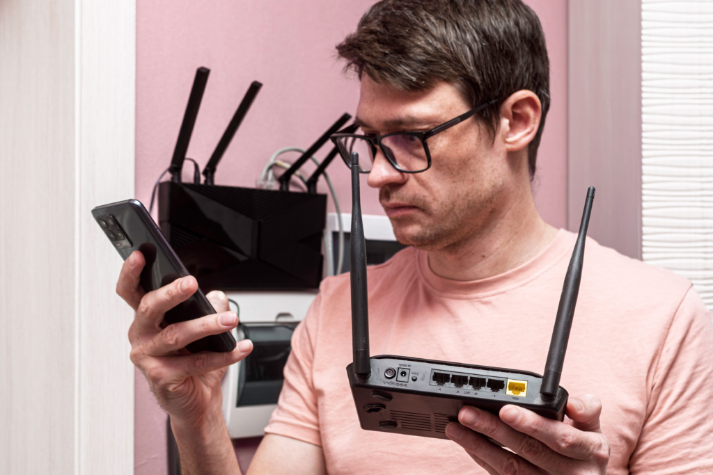 A man is holding a wifeless router in one hand and looking up what he needs for Usenet on his phone with the other.