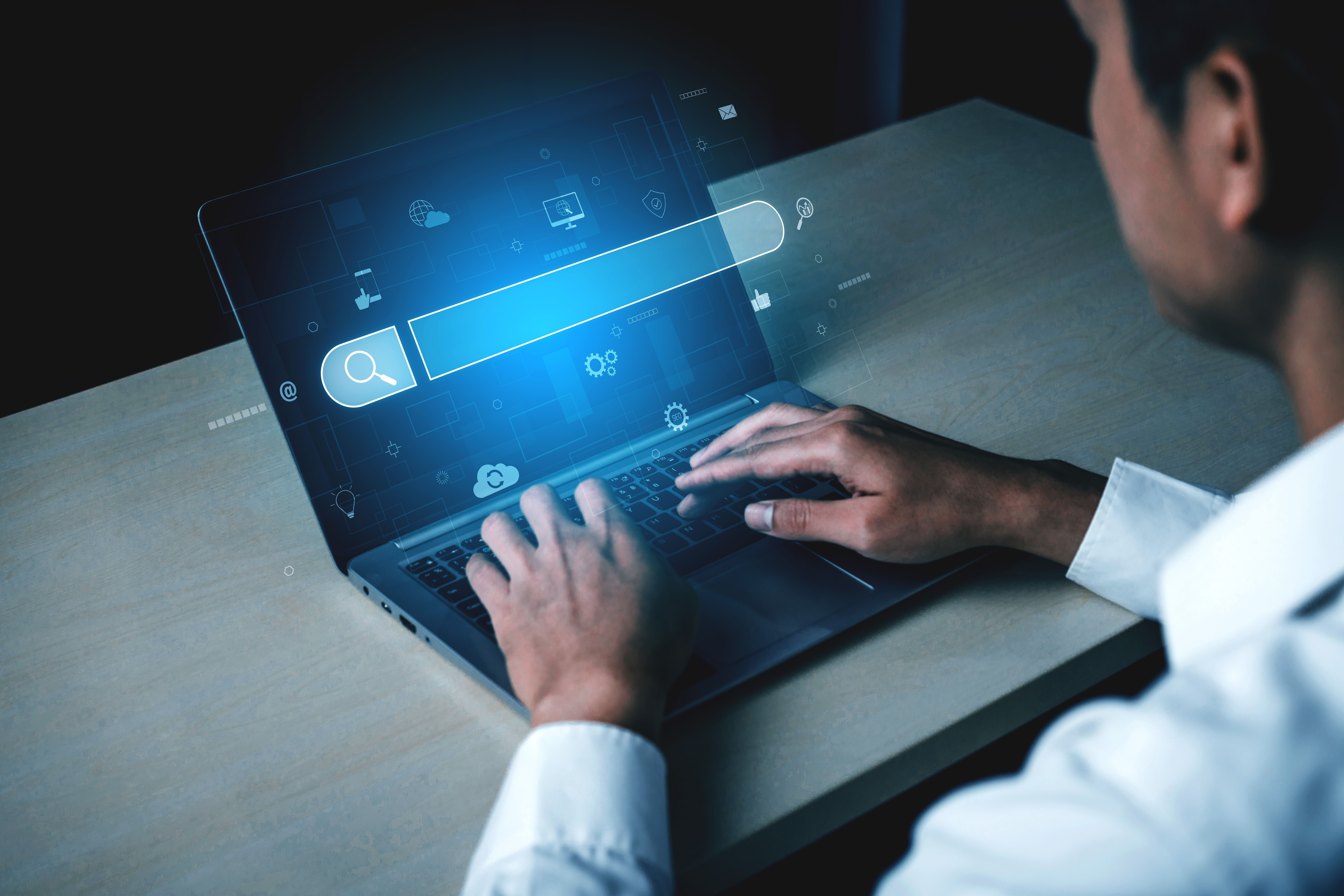 A person is typing on a laptop and a hologram of a Usenet search bar is hovering in front of the screen.