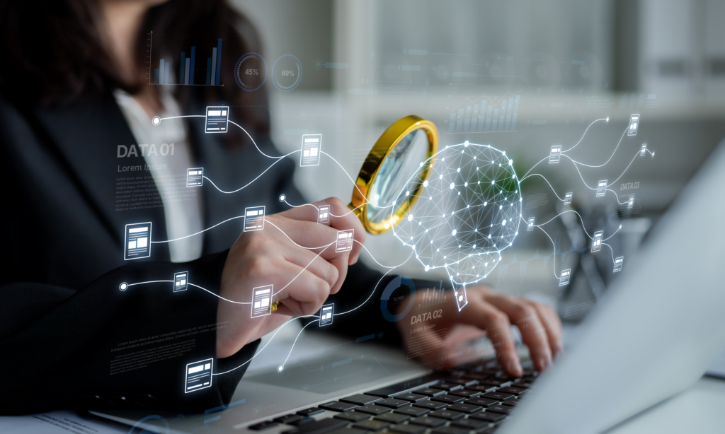 A person is sitting behind a laptop looking at the hologram of a brain attached to various files. She is holding a golden magnifying glass.